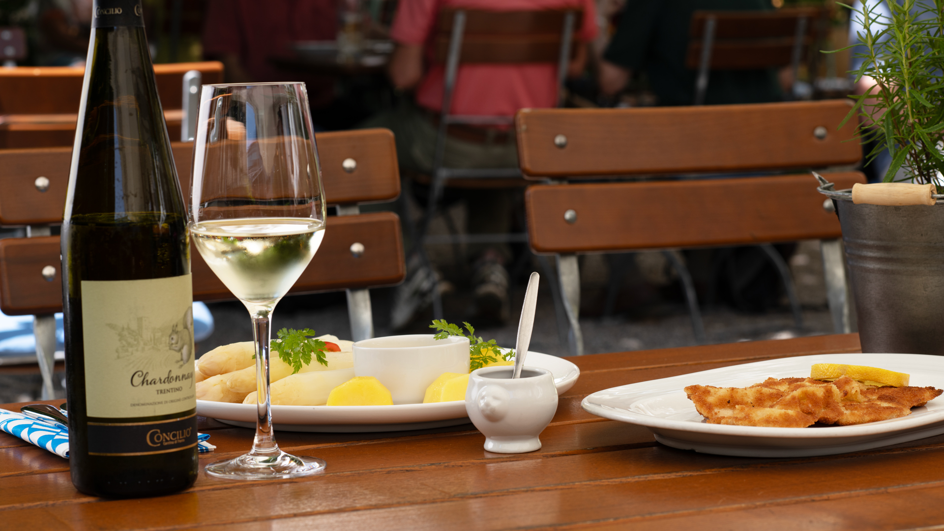 Spargel mit Sauce Hollandaise und Schnitzel, dazu eine Flasche und Glas mit Chardonnay, davon ein Töpfchen mit flüssiger Butter.