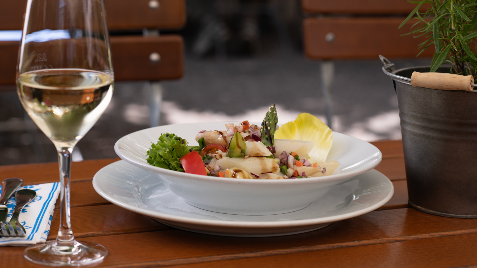 Ein tiefer Teller mit einem sommerlichen Spargelsalat mit grünem und weißem Spargel, Blattsalaten, Zwiebeln, Tomaten und einer Sauce mit Balsamico.